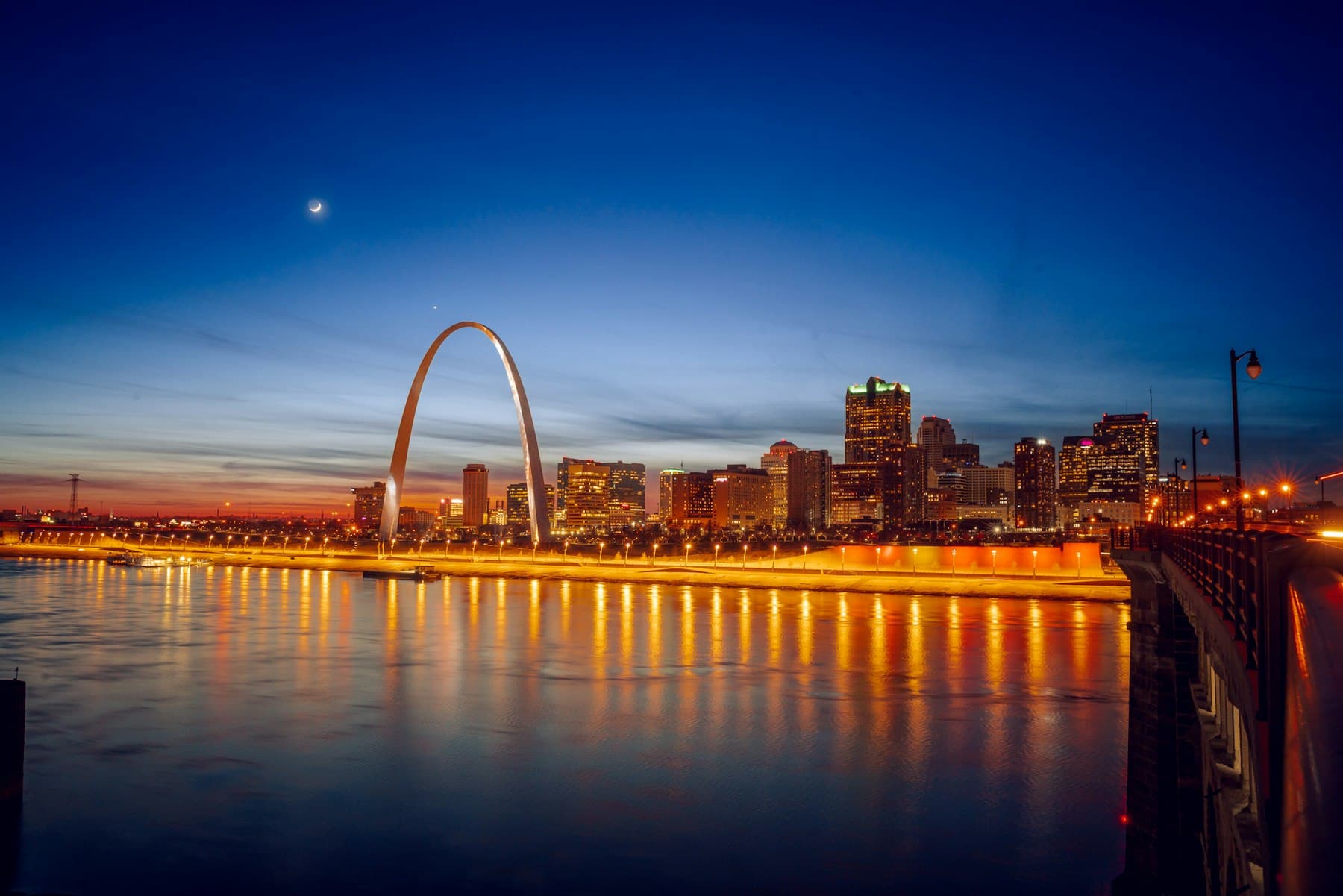 St. Louis skyline at sunset with the Gateway Arch reflected on the Mississippi River.