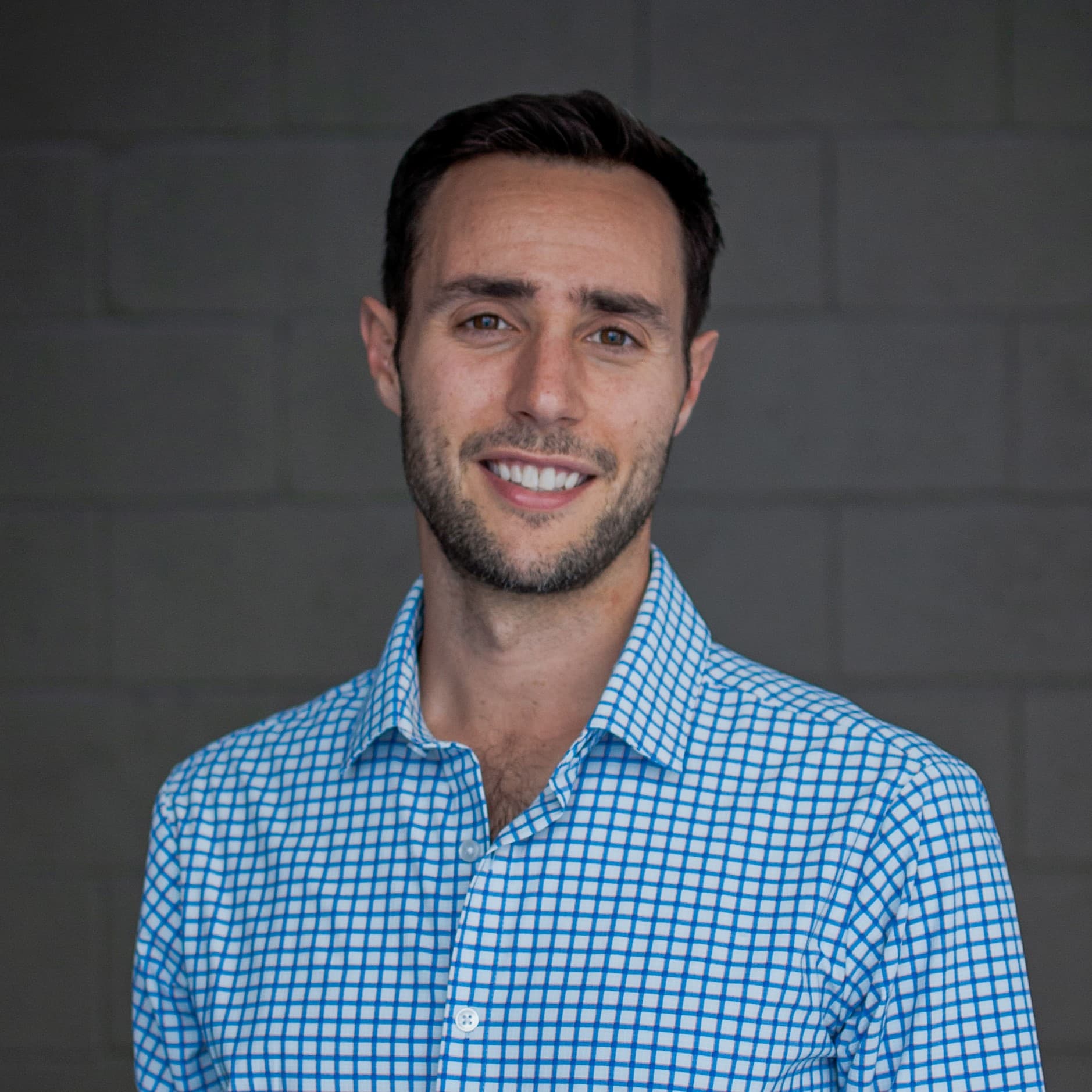 Greg Stahl, founder of Water Co, smiling against a gray brick wall.